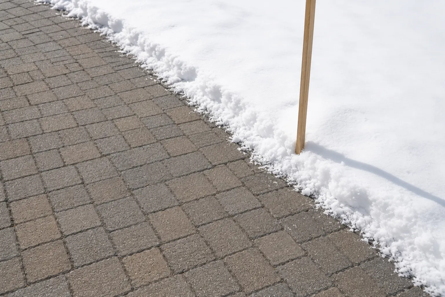 Interlock paver driveway edge staying intact beside snow in an Ottawa winter.