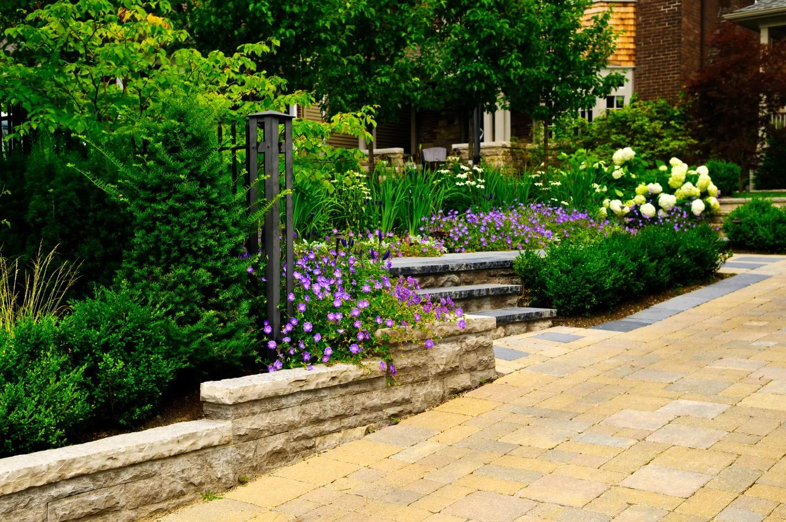 Interlocking paver walkway with stone retaining wall and flower beds in an Ottawa front yard.