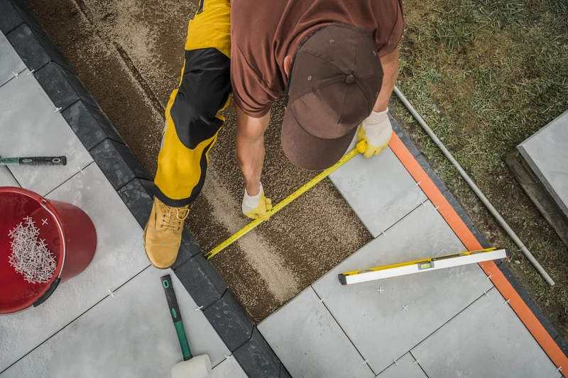 A contractor measures and aligns paving stones during a paving stone installation in Ottawa.