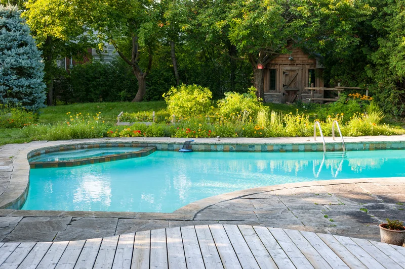 Pool deck paving stones curve around a backyard swimming pool bordered by garden beds in Ottawa..