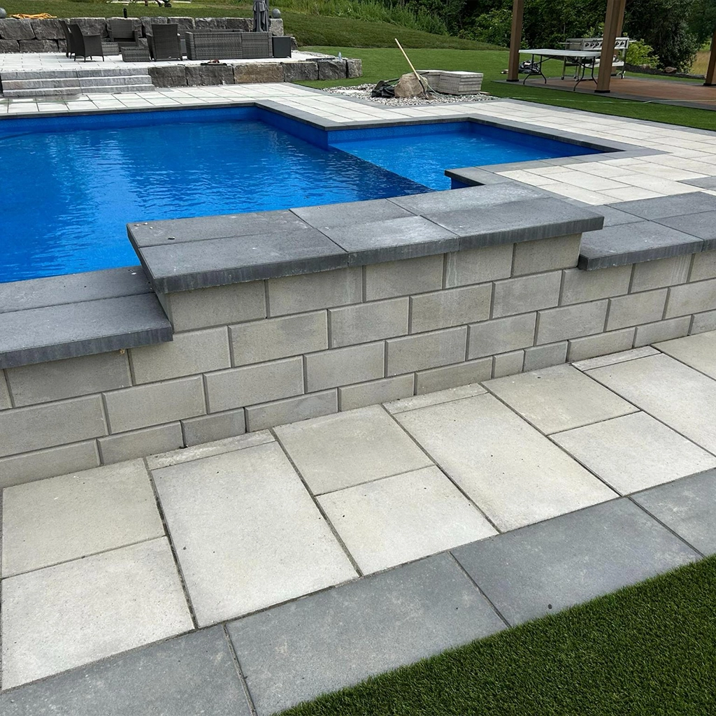 Pool deck paving stones form a multi-level surface with a raised retaining wall in an Ottawa backyard pool area.