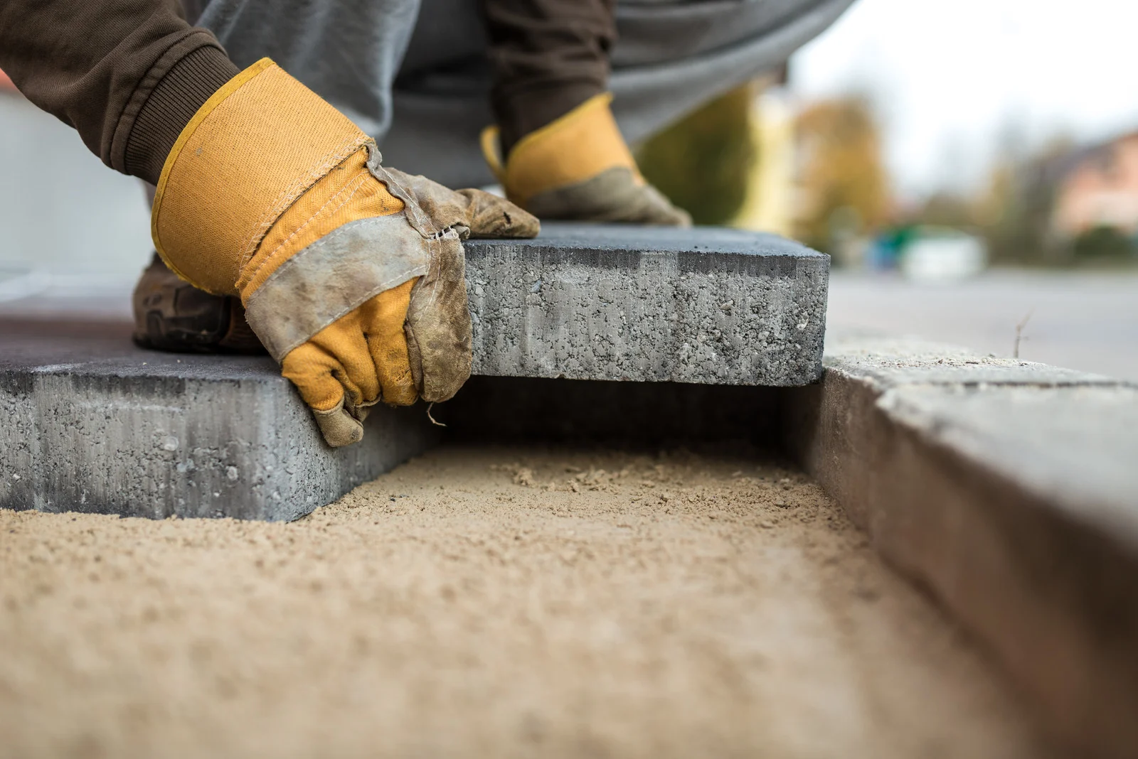 Walkway Installation Ottawa – installer setting a paver on a compacted sand base.